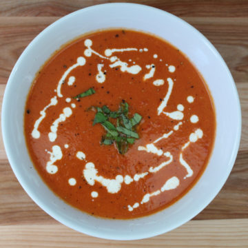 Bowl of tomato soup drizzled with heavy cream, black pepper, and basil
