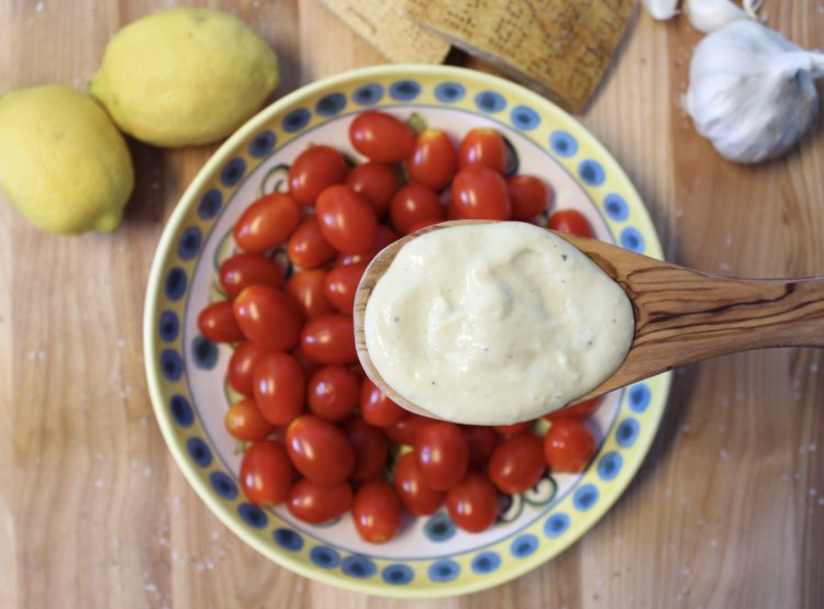 Wooden spoon with Caesar dressing held over plate with cherry tomatoes