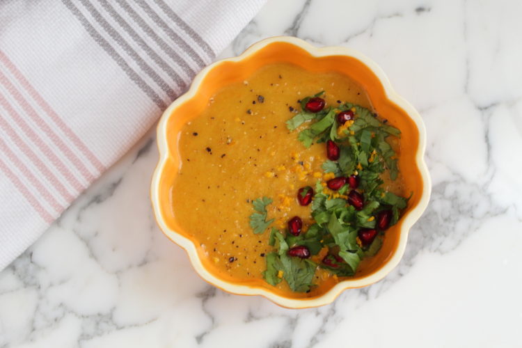 Pumpkin soup in pumpkin looking bowl topped with cilantro, pomegranate, orange zest