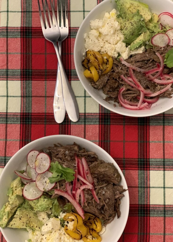 Two bowls with vegetables, meat and cheese on Christmas placemat and two forks