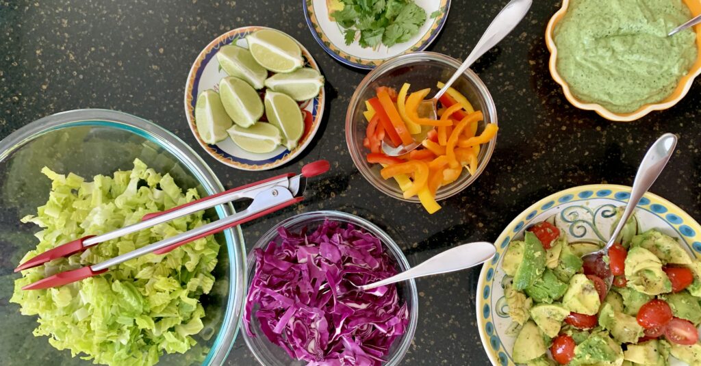 Various taco bowls toppings: lettuce, avocado, vegetables, lime, bell peppers