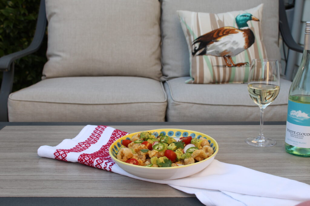 Patio table set with pork rinds nachos, glass of white wine